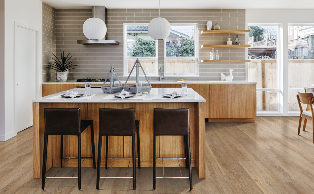 light wood-look flooring in modern kitchen with light wood cabinets with white stone countertops and a tan subway tile backsplash 